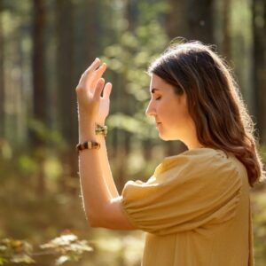 Frau in gelbem Oberteil bei einer achtsamen Übung mit erhobenen Händen im sonnigen Wald beim Yoga Wochenende von Vivere Vital