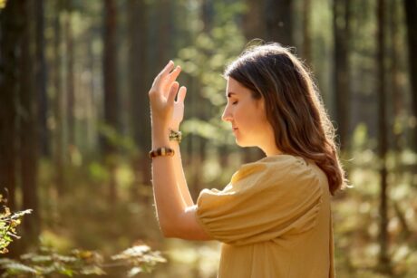 Frau in gelbem Oberteil bei einer achtsamen Übung mit erhobenen Händen im sonnigen Wald beim Yoga Wochenende von Vivere Vital